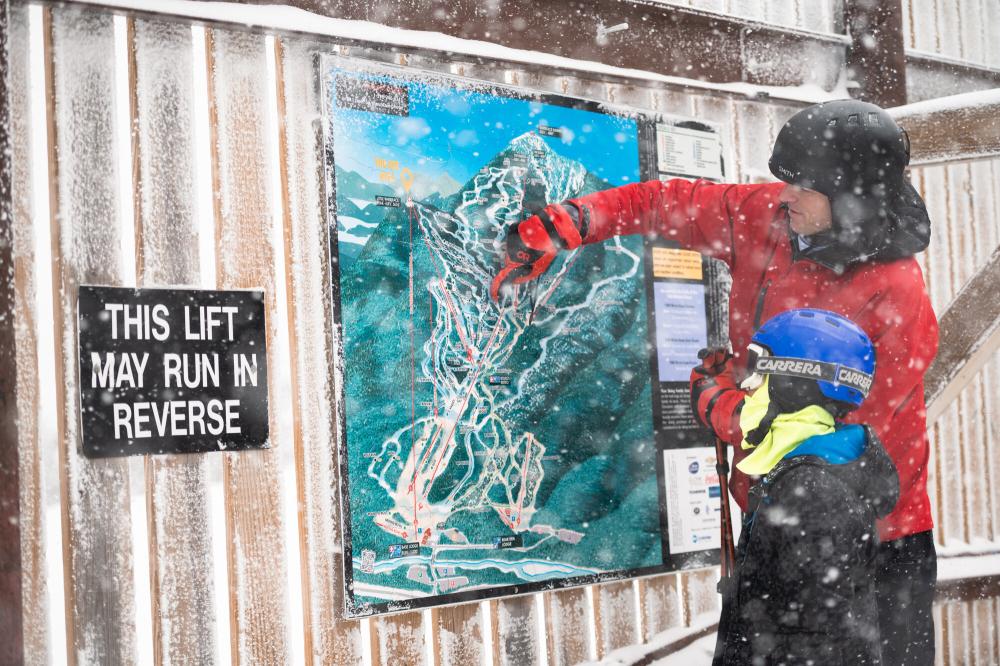 A father pointing out something on a ski mountain map to his kid