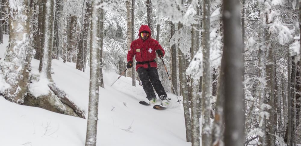 Ski patroller in a red coat skiing through the trees