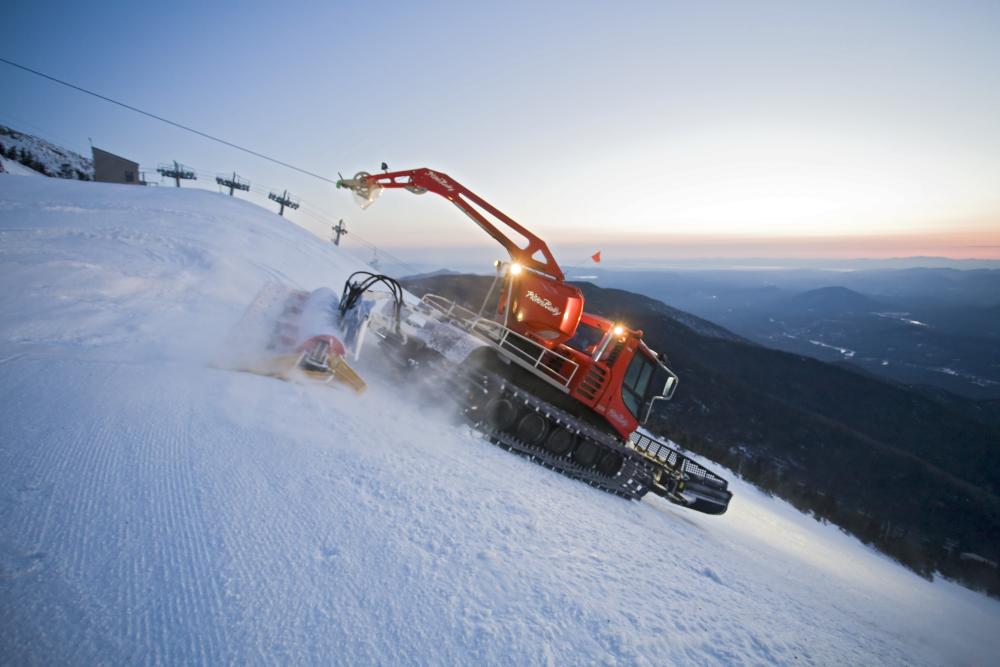 A large snow-grooming machine works its way down a snowy mountain.