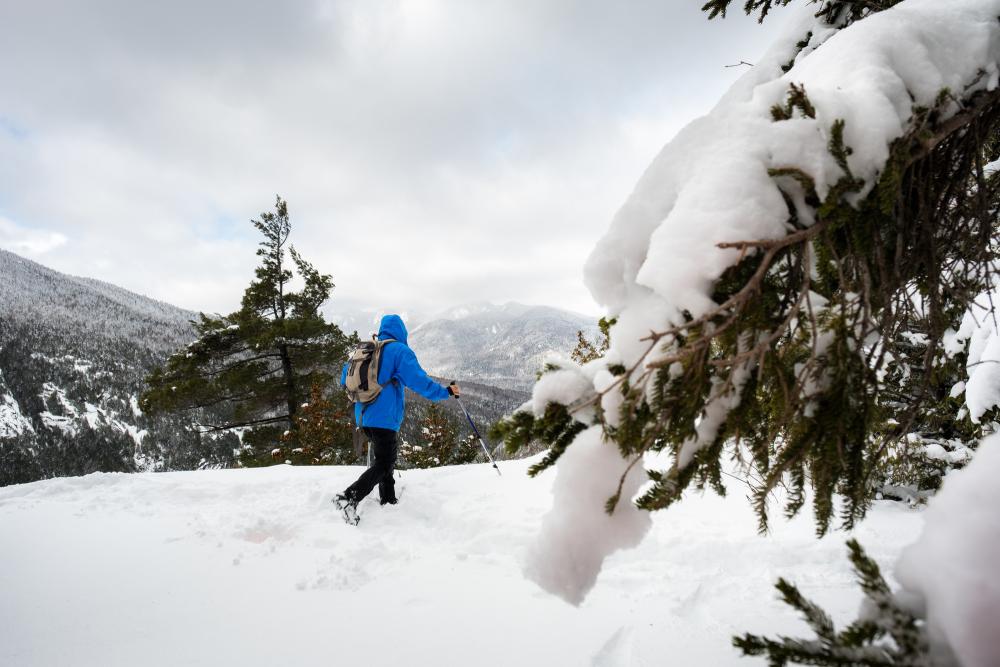 A man walks through thick snow in a bright blue jacket, using walking sticks.