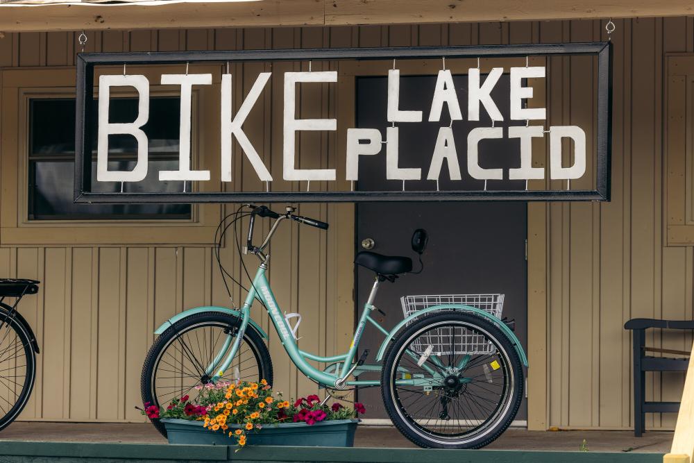 The porch of a bike shop. The sign reads "Bike Lake Placid" over a bright blue cruiser bike.