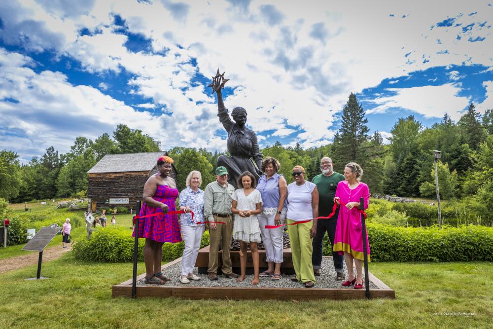 A group of people cut the ribbon on a new Harriet Tubman statue at John Brown Farm.