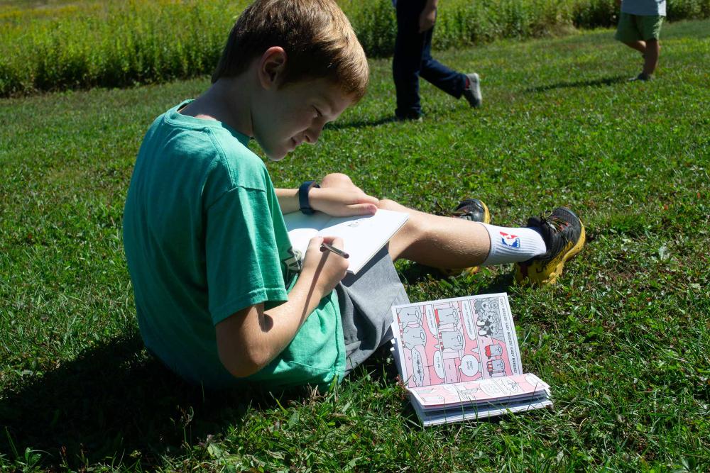 A young boy reads a book on the grass.