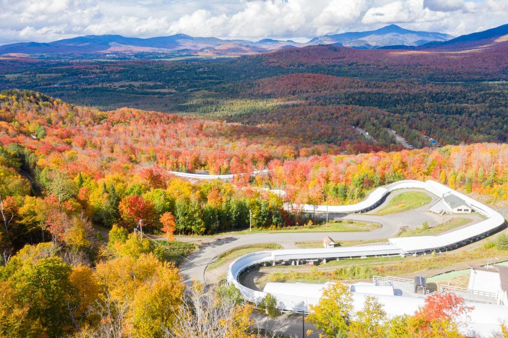 An aerial view of the Cliffside Coaster course at Mt Van Hoevenberg with fall foliage and mountains in the background.