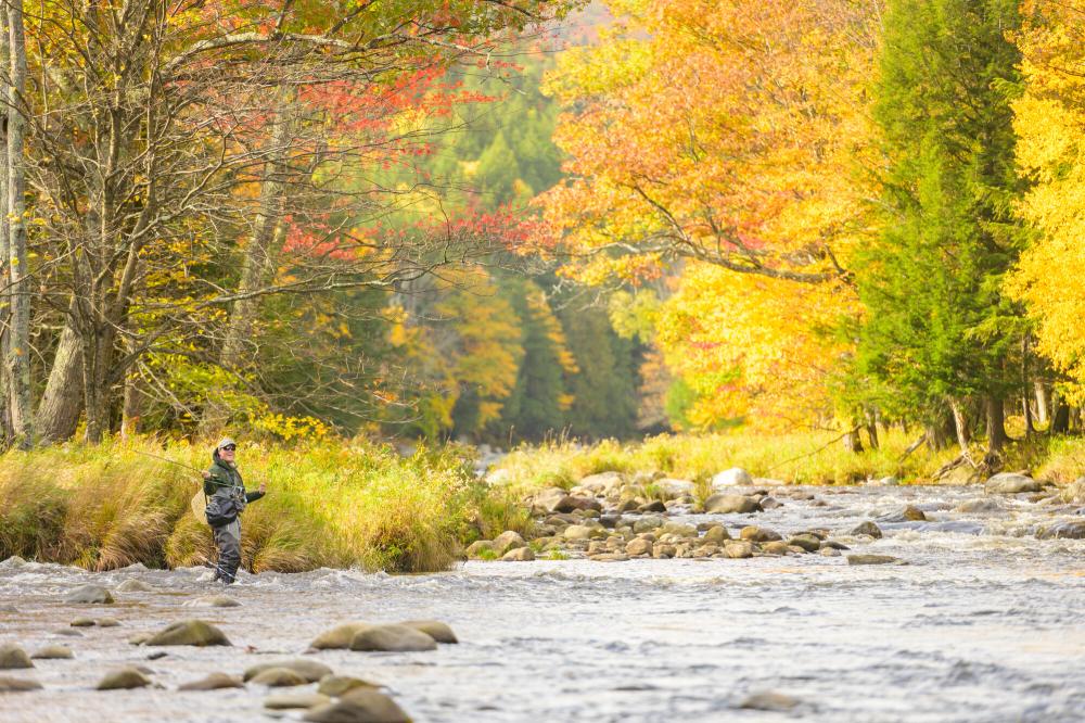 A man smiling while fly fishing and standing in the Ausable River.