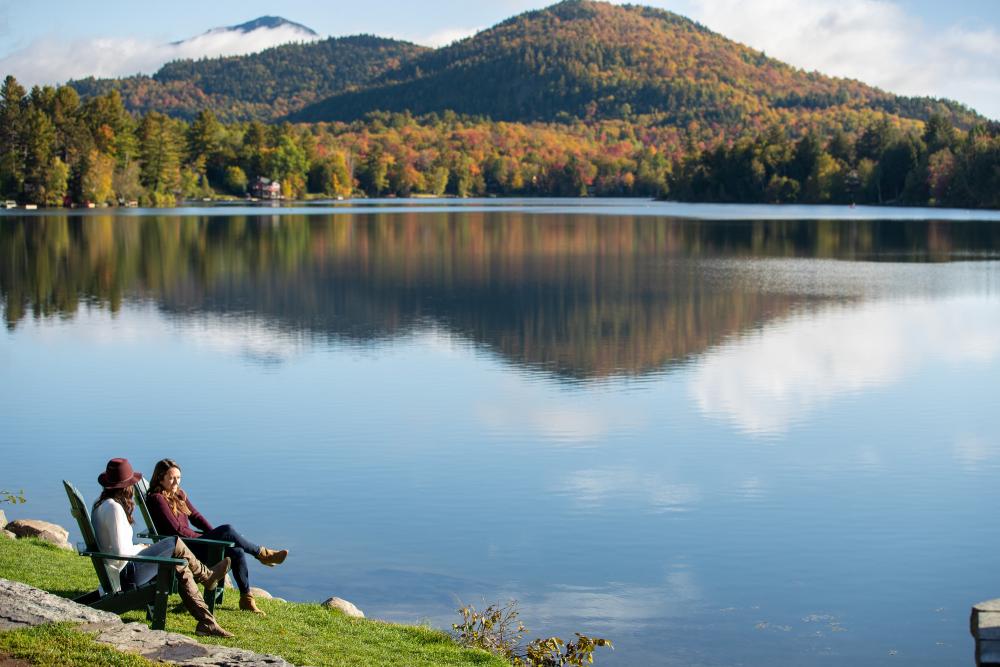 Two women sit at the edge of Mirror Lake with fall views