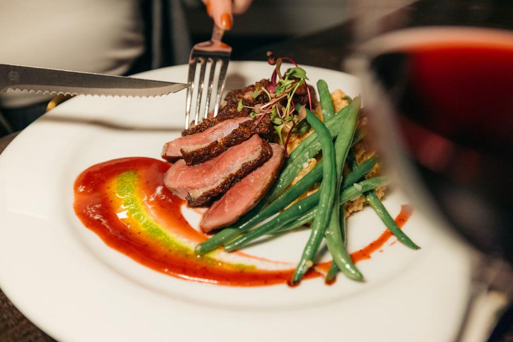 Fork and knife cutting into meat, quinoa, and green bean dish