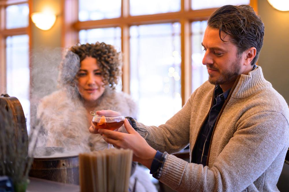 Man pulls cocktail from smoking box at bar as woman looks on