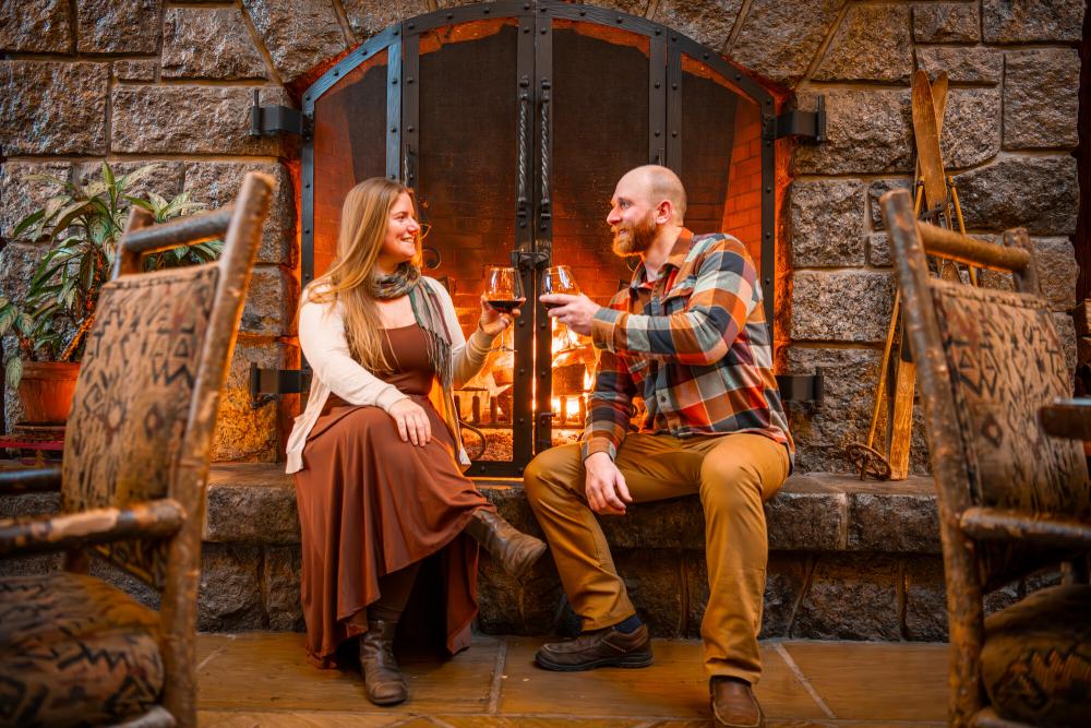 Man and woman cheers glasses sitting in front of stone fireplace