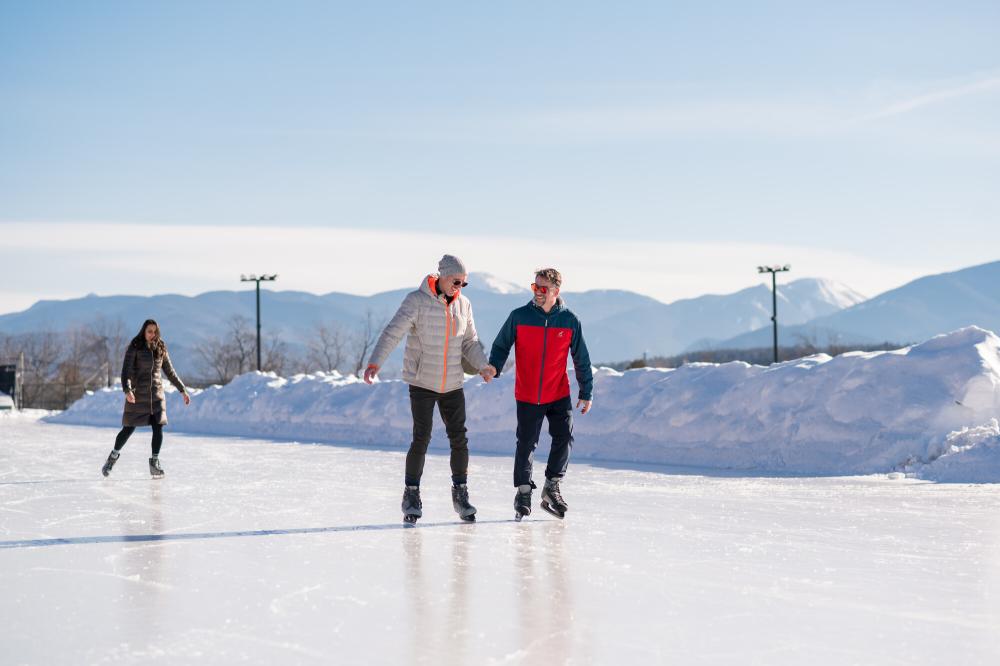 Two men ice skate on outdoor track holding hands