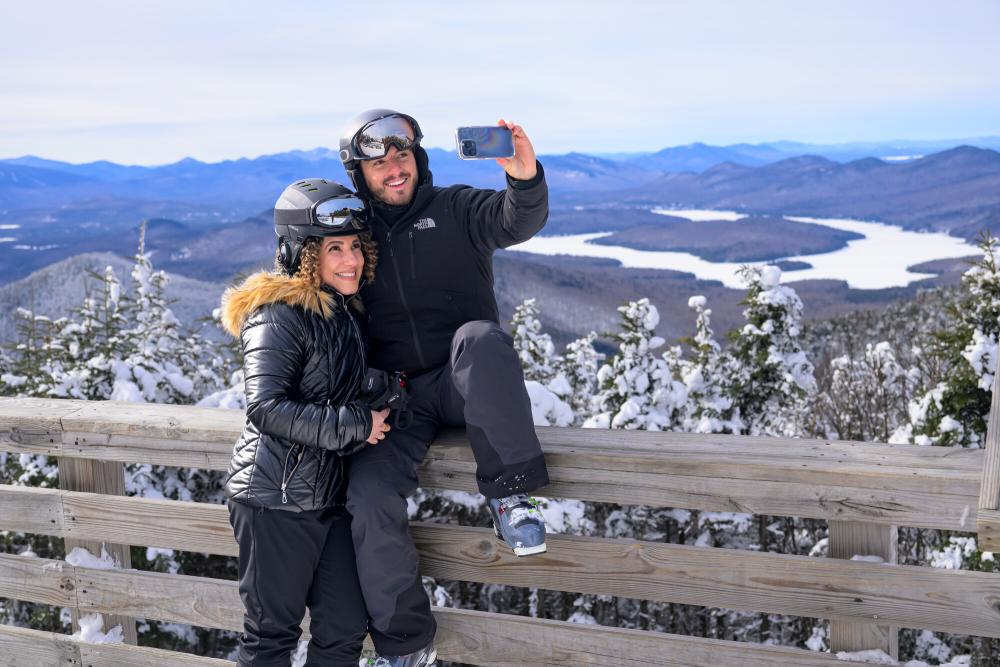 Man takes selfie of himself and woman in ski gear on mountain observation deck