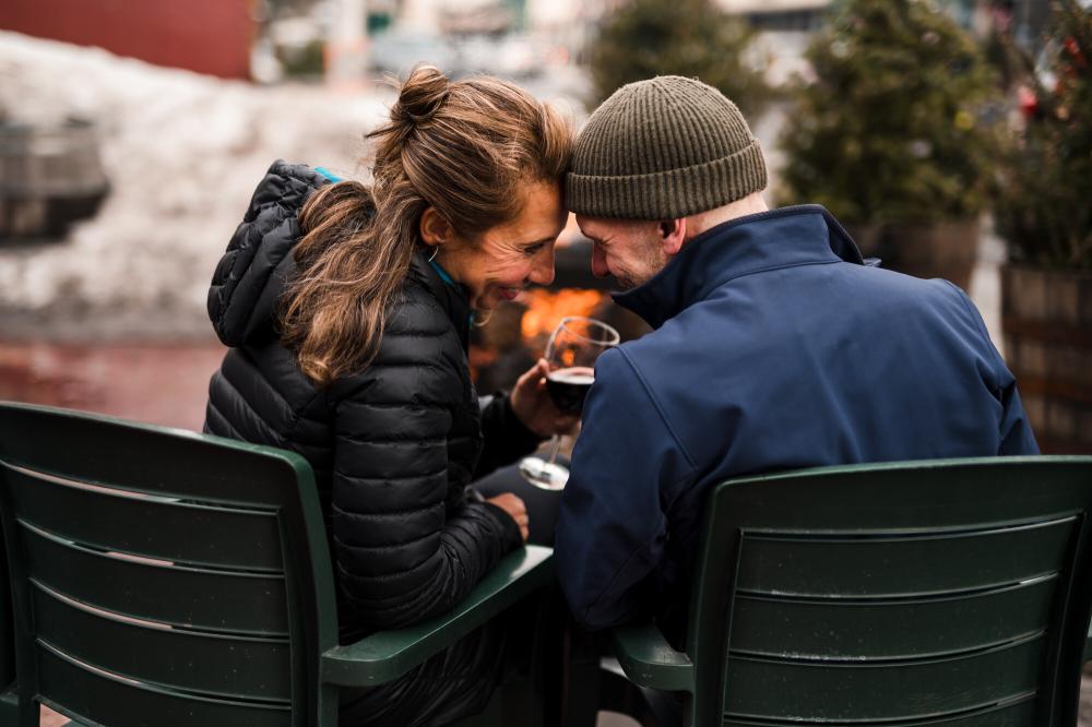 Couple sit head to head in Adirondack chairs by fire