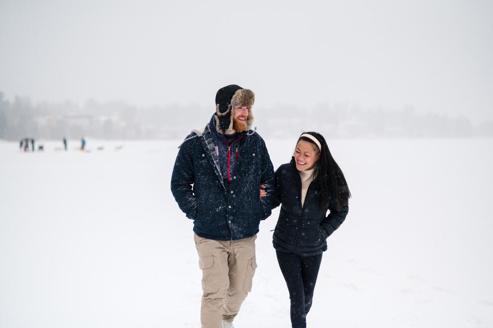 Man and woman walk arm and arm on frozen lake in snowstorm