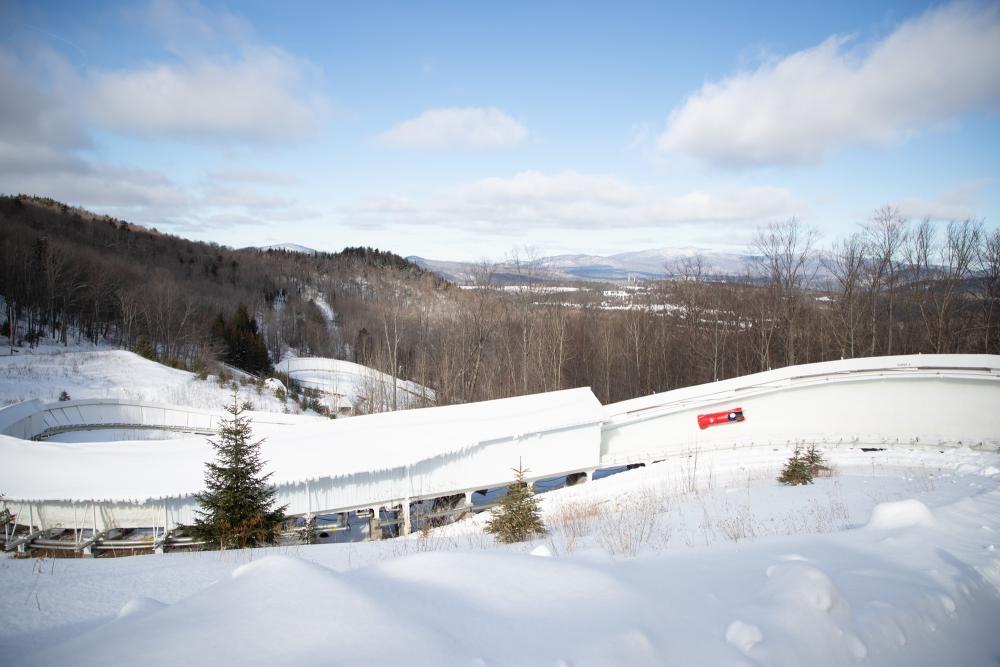 Red bobsled slides down track with mountains in background