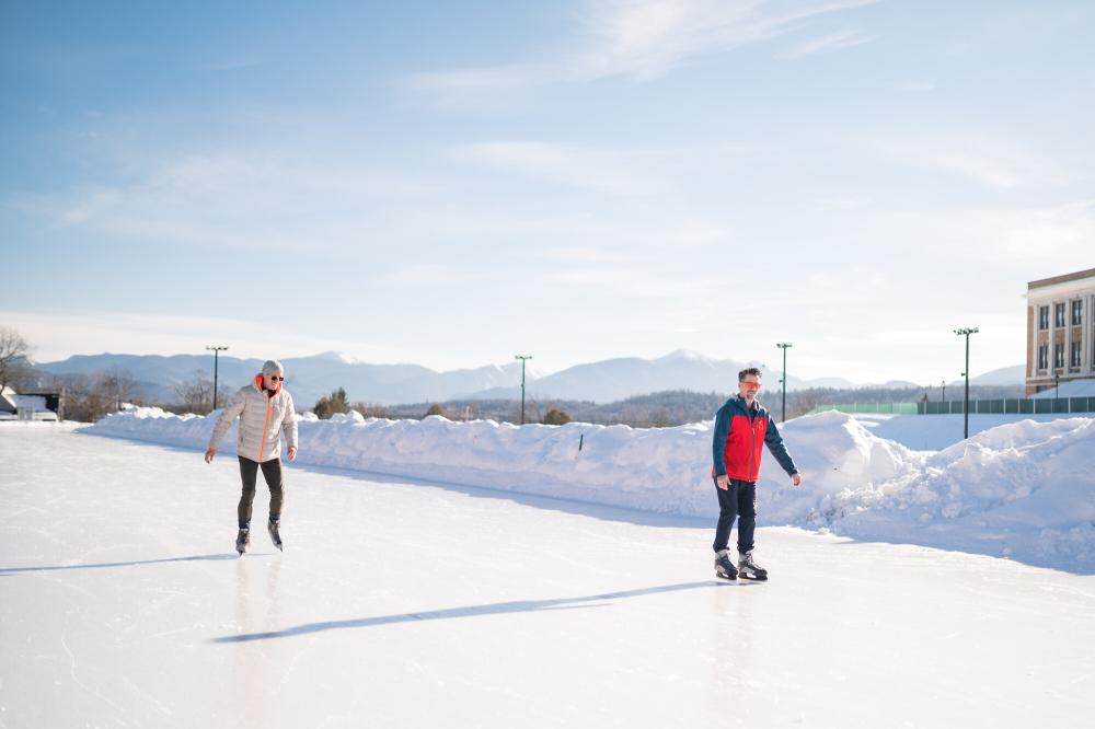 Two men ice skate on Olympic Oval on snowy bluebird day