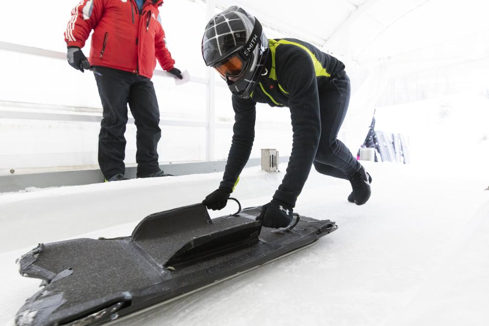 Person in helmet runs down track with skeleton sled in hand