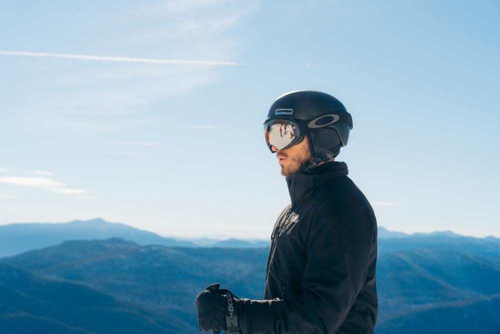 Man looks at view from top of mountain wearing ski helmet and goggles