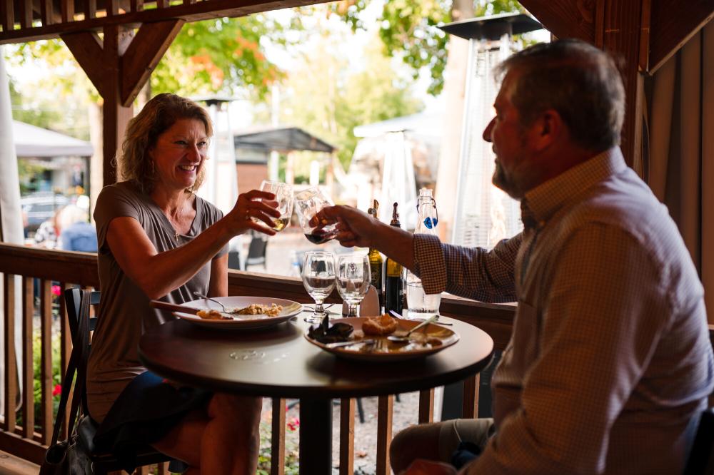 A couple sitting on a patio, smiling and raising their glasses at Amado restaurant.