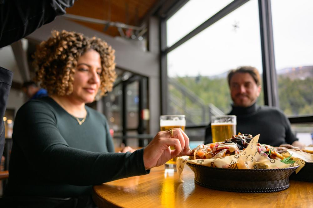 A woman with very curly hair takes a bite from nachos.