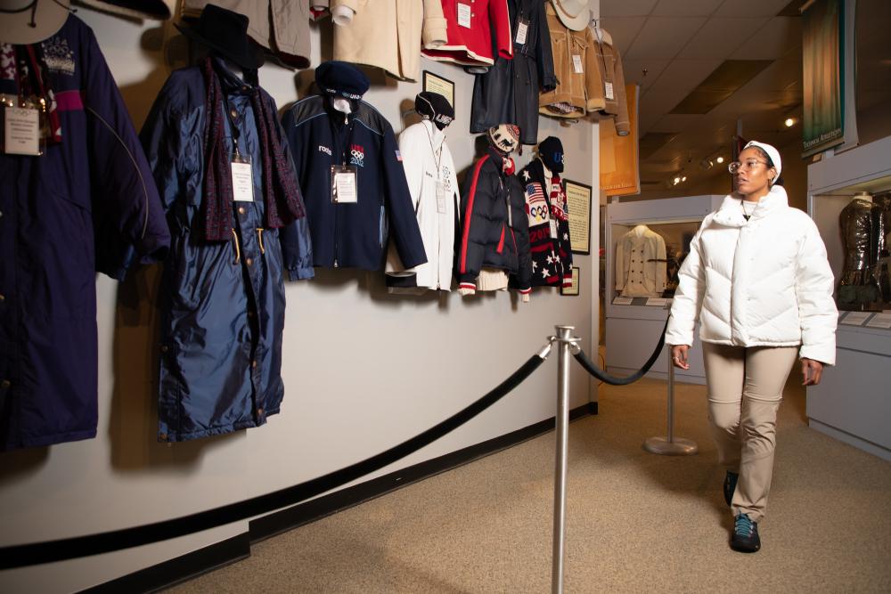 A woman in a white winter coat looks at vintage Olympic clothing.