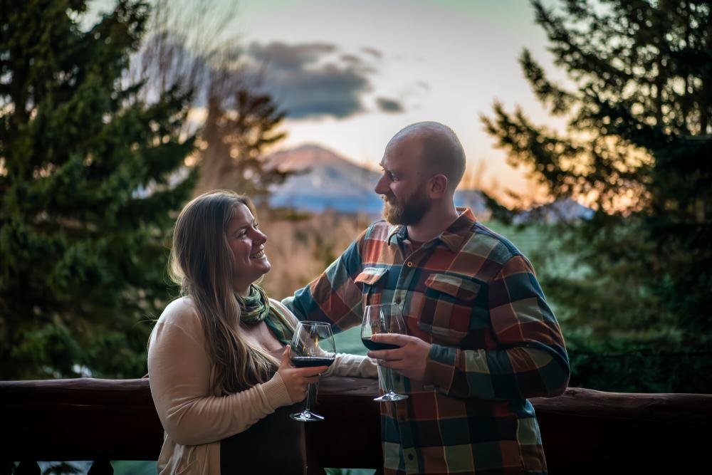 A man and woman toast drinks on a snowy balcony.