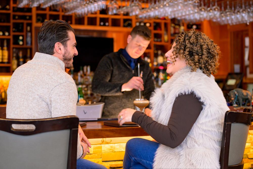 A man and woman enjoy drinks and food at a bar.