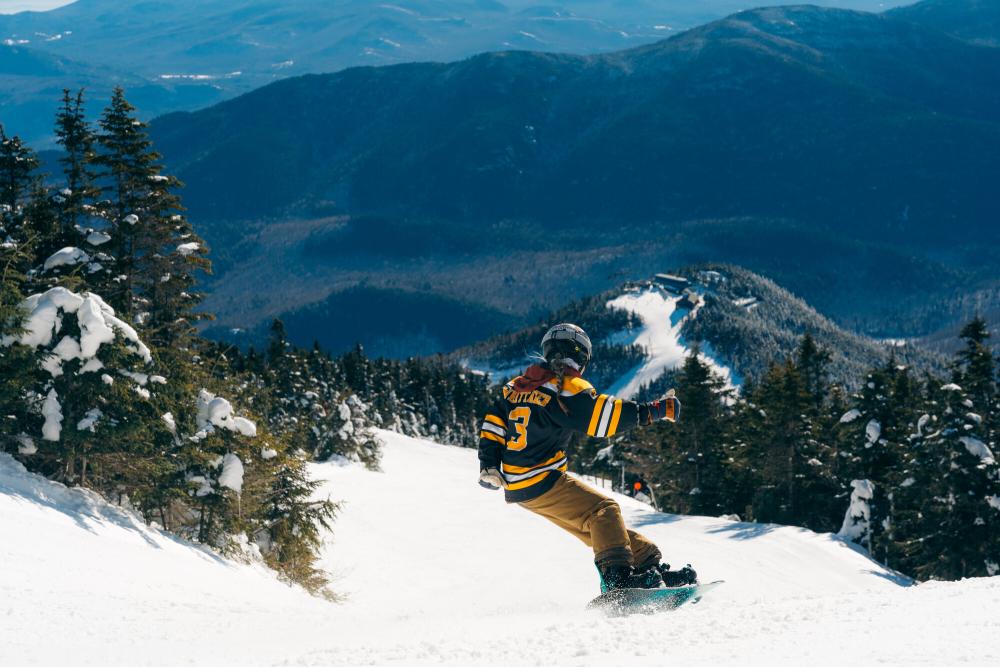 A woman in a bruins jersey snowboards down a mountain.