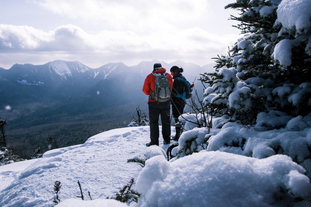 Two people in outdoor gear stand on the side of a mountain.