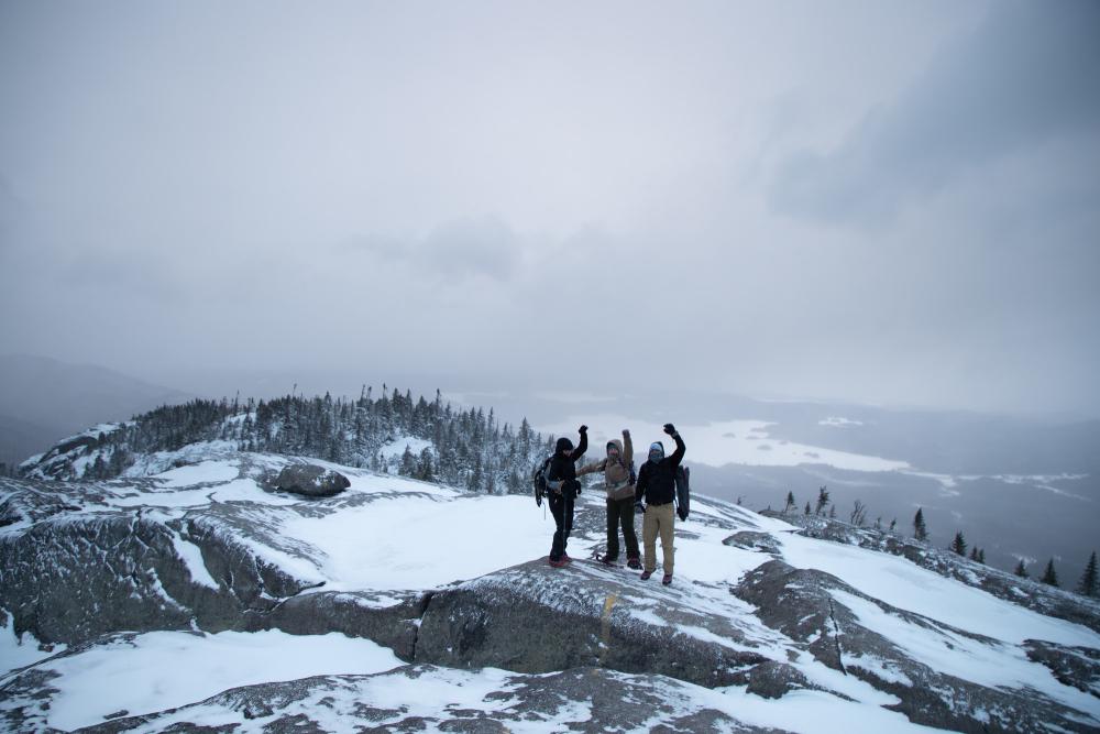 A group of hikers pose for a photo on top of Ampersand Mountain in the winter