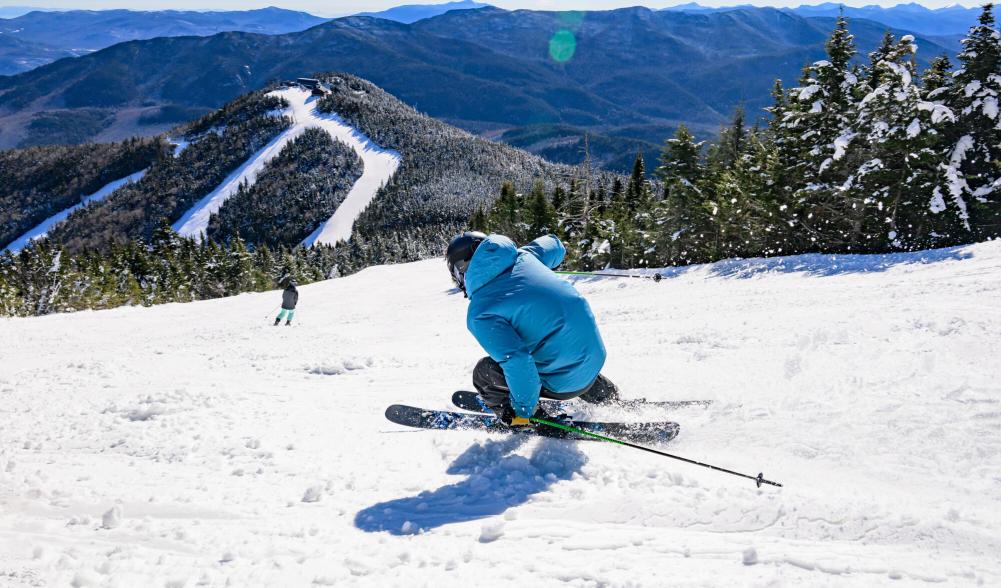 A skier in a blue puffy shredding down the mountain