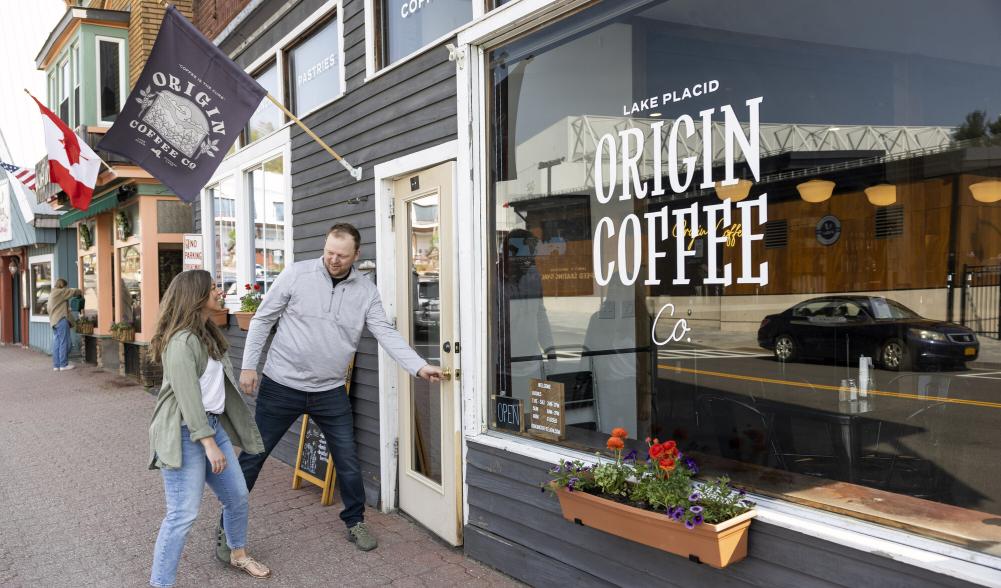 Man opening door of Origin Coffee shop looking back at woman