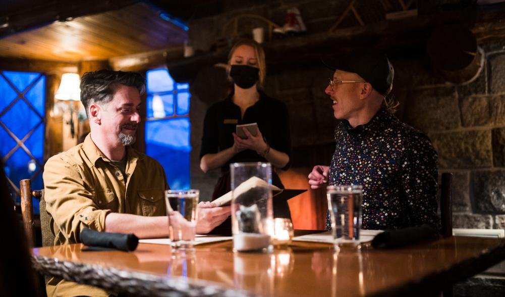 Two men sit in a cozy, dimly-lit rustic dining room at a luxury resort.