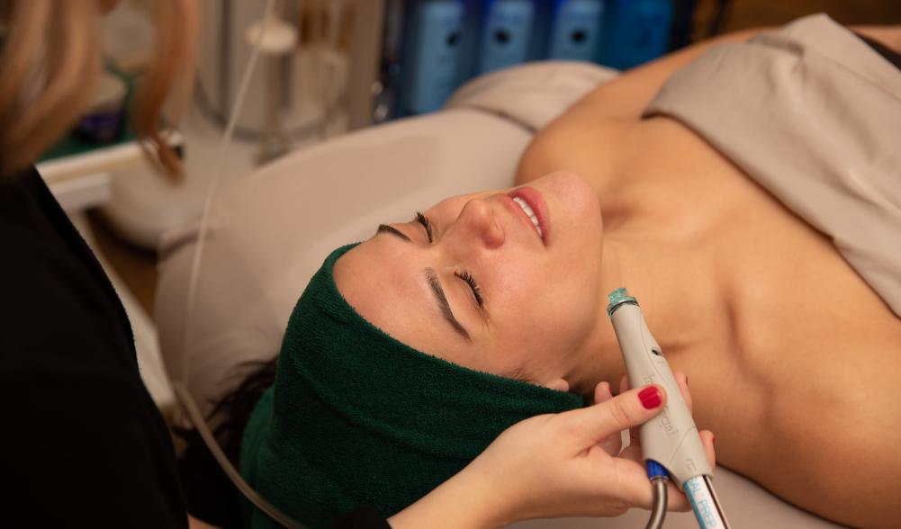 A close-up of a woman with her hair wrapped in a towel, eyes closed, receiving a relaxing spa treatment.