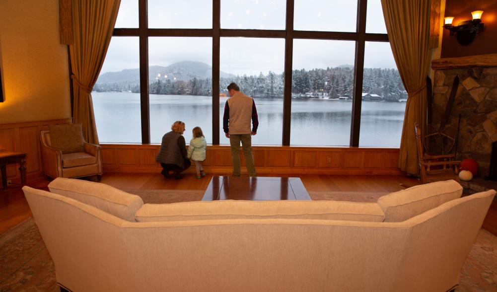 A man, woman, and small child look out at a lake through two-story windows.