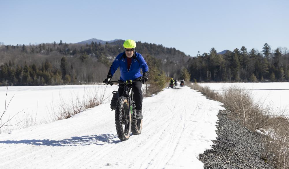 A man riding a fat tire bike over a thin snow trail.