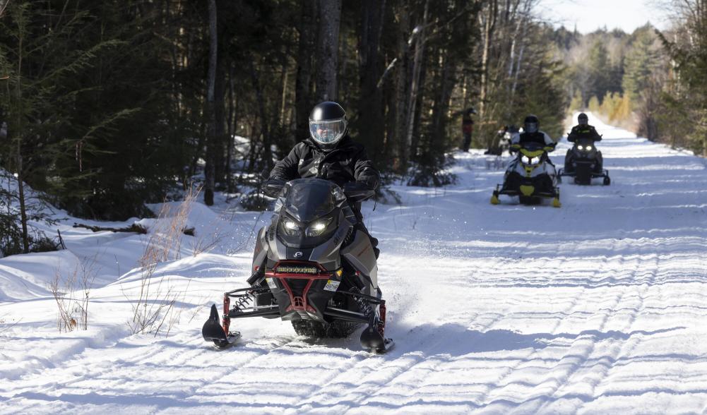 A group of snowmobilers ride along a snowy trail.