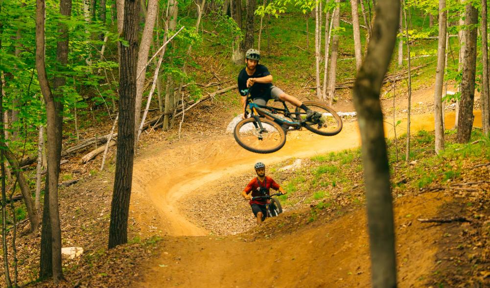 A mountain biker flies through the air off a jump in the woods.