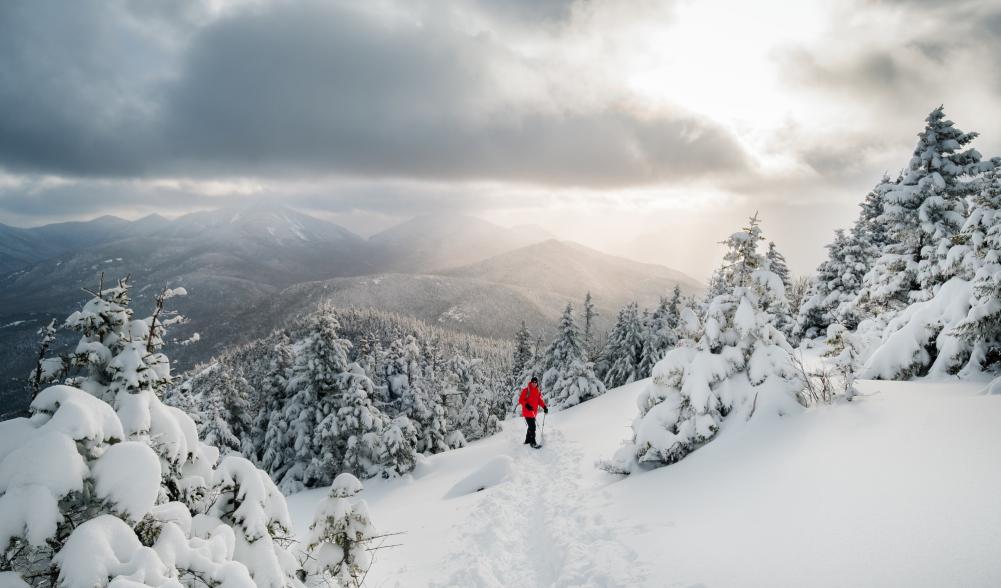 A person snowshoeing up a mountain in Keene during the winter with stunning mountain views in the background.