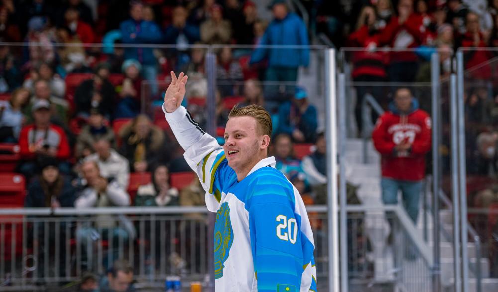 A male hockey player in uniform waves to fans from the ice.