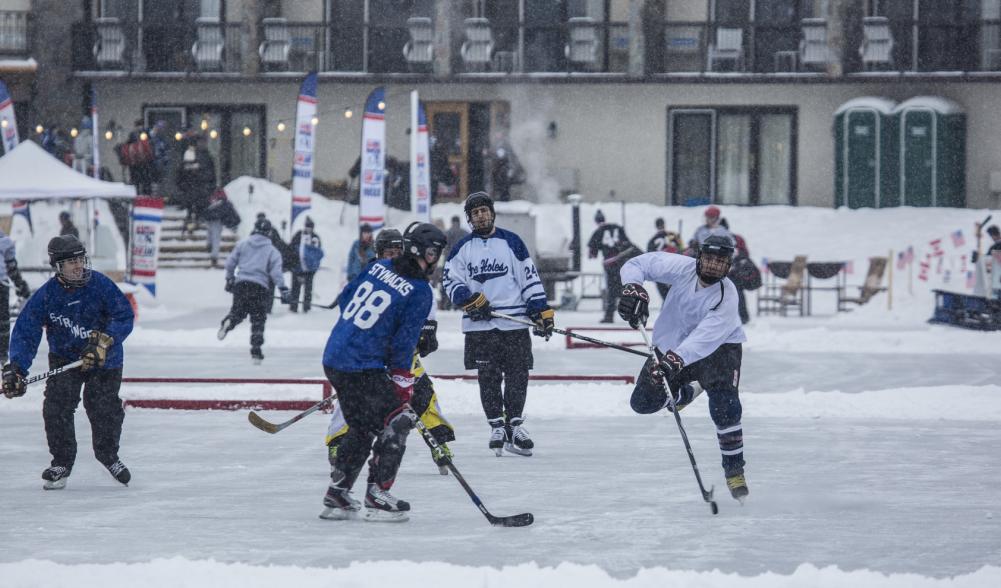 Pond hockey players compete on a snowy day at an outdoor rink.