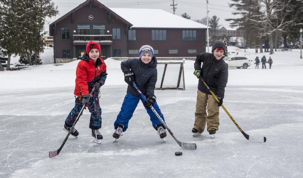 Three small boys pose with their sticks and a puck at lake rink.