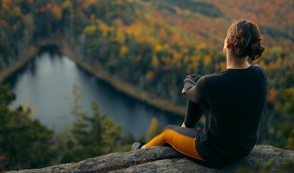 A woman sits on a rock overlooking fall foliage mountain views.