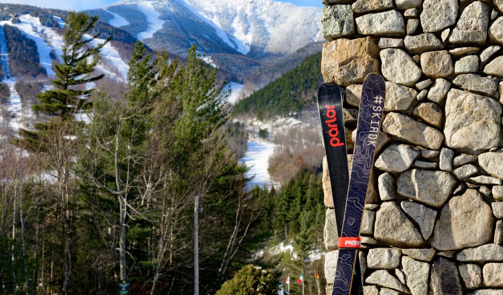 Skis propped against stone wall with Whiteface trails visible in background