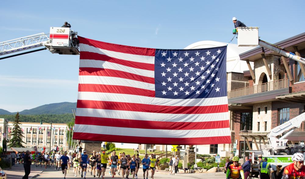 Two cranes hold up a large American flag over a marathon route through town.