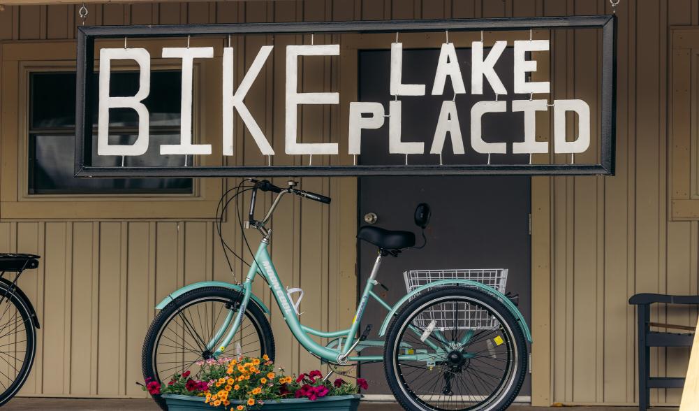 The porch of a bike shop. The sign reads "Bike Lake Placid" over a bright blue cruiser bike.