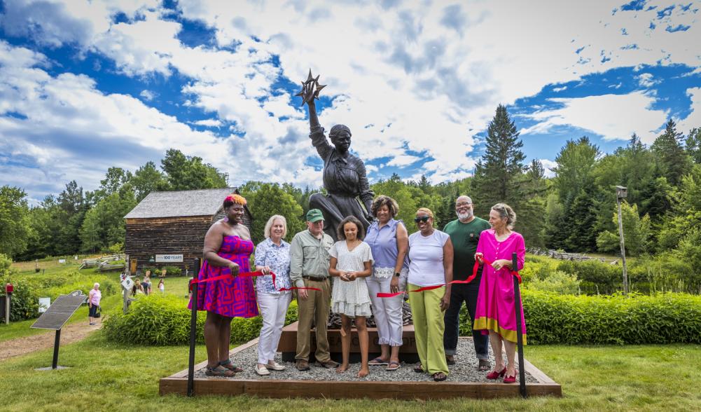 A group of people cut the ribbon on a new Harriet Tubman statue at John Brown Farm.