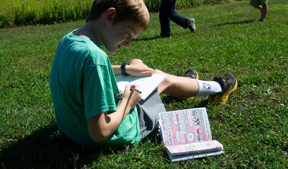 A young boy reads a book on the grass.