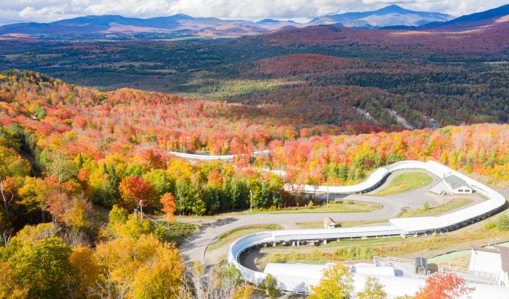 An aerial view of the Cliffside Coaster course at Mt Van Hoevenberg with fall foliage and mountains in the background.