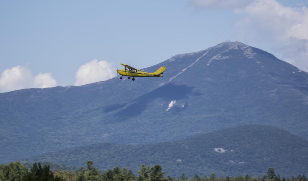 A yellow airplane in flight with mountains in the background.