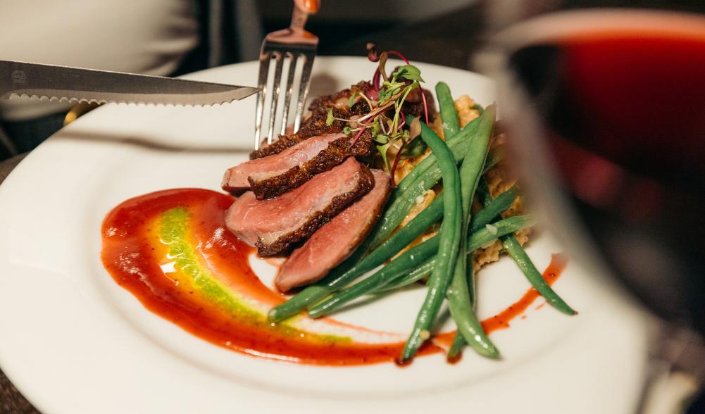 Fork and knife cutting into meat, quinoa, and green bean dish